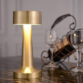 Gold table lamp on a marble surface with wine glasses and bottles in the background